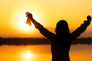 Fototapeta premium Silhouette of Hope, Positive Mind for Coronavirus Concept. Woman hand Raised Up a Medical Mask. Gesture means Goodbye. Take-Off Mask and Deep Breathing for Fresh Air