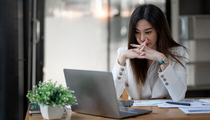 Obraz premium Tired caucasian business woman feeling stressed from hard work, sitting at office desk and looking at laptop screen.