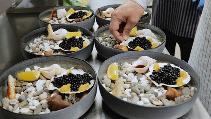The chef decorates a dish with crab and black caviar. Seafood dish served on stones. Restaurant kitchen, the chef prepares a signature dish