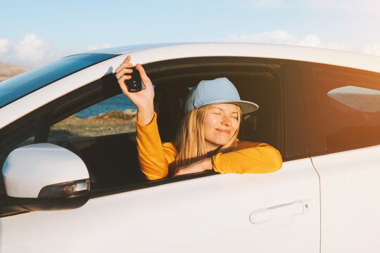Woman driver in a new car showing keys in open window. Girl buying auto. Road trip travel vacations transport insurance concept.
