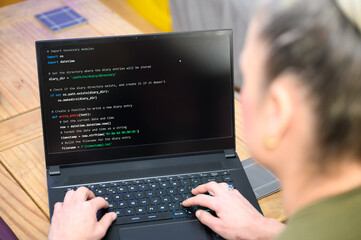 Coding in the house, a woman writing code on a laptop for an app or website while working from home