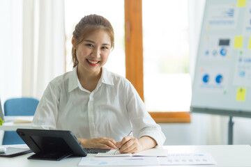 Looking camera, Attractive asia employees in successful modern office, Financial graphs on her workstation. Young asian freelance employee online marketing ecommerce telemarketing concept report