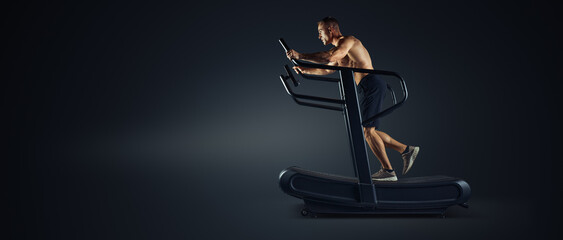 Fototapeta na wymiar Running on treadmill. Muscular male athlete in sportswear running on professional treadmill, Jogging machines sideview studio shot