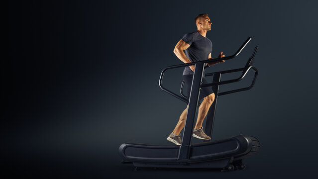 Man running. Athlete Training on Curved Sprint Treadmill. Walking or jogging workout. Studio shot on black.
