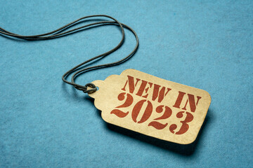 new in 2023 - red stencil text on a paper price tag against blue paper, business marketing concept
