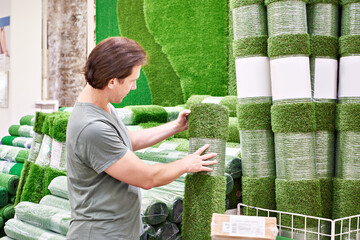 Man buying rolls of artificial grass turf in store