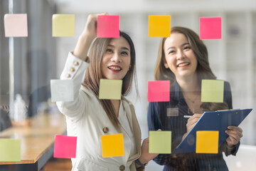 Team of Business female employee with many conflicting priorities arranging sticky notes commenting and brainstorming on work priorities colleague in a modern office.