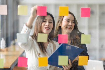 Team of Business female employee with many conflicting priorities arranging sticky notes commenting and brainstorming on work priorities colleague in a modern office.