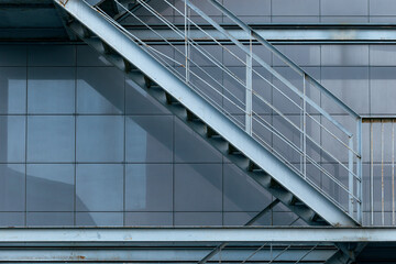 Close-up of a metal fire escape staircase, facade of building in grey metal tiles.