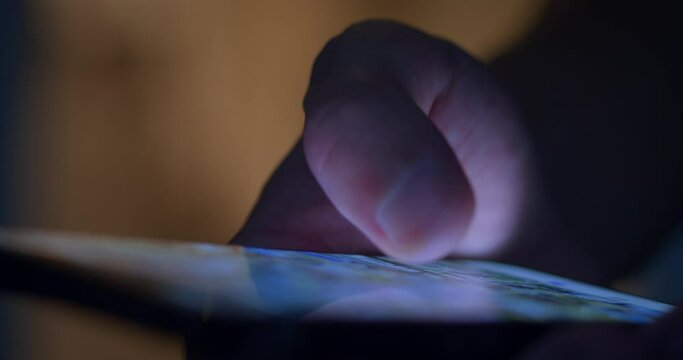 Close-up: male hand using smartphone at night at the table indoors.
