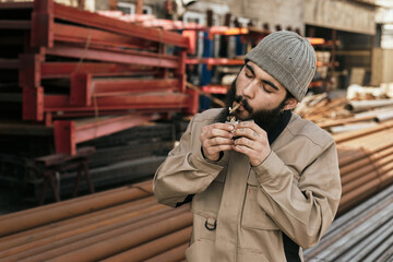 Waist up portrait of bearded man in workwear lighting up cigarette on break