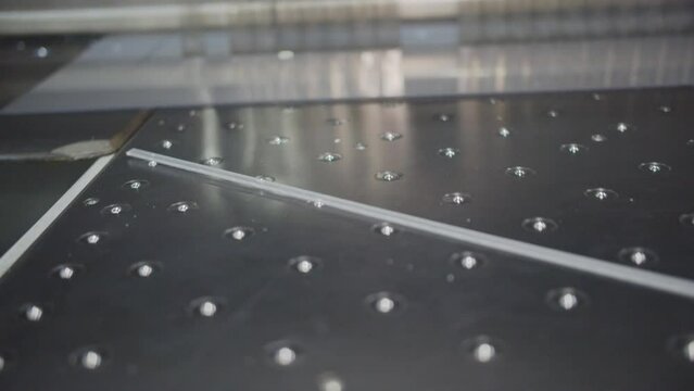 Machine cuts polycarbonate panels at factory. Small scrap separates from transparent sheet. Automatic equipment at modern industrial production closeup