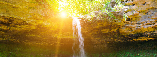 Beautiful waterfall in the forest and sun. Wide photo.
