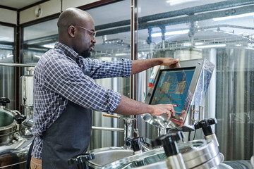 African American engineer controlling equipment with computer monitor during his work at brewery