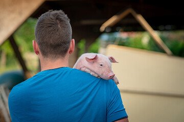 Kleines Ferkel liegt auf einer Schulter, eines jungen Landwirtes. © Countrypixel
