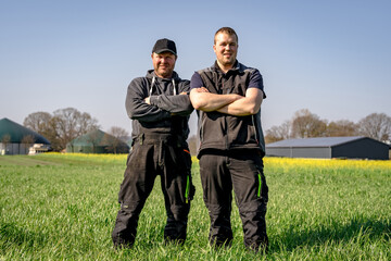 Landwirt und sein Sohn stehen auf einem Feld vor einer Biogasanlag im Hintergrund und blickt...
