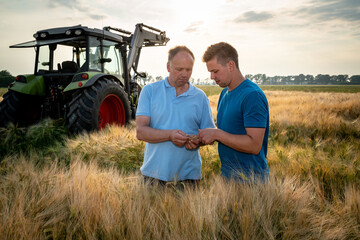 Landwirt mit seinem Sohn im reifen Getreidefeld, im Hintergrund steht ein Traktor.