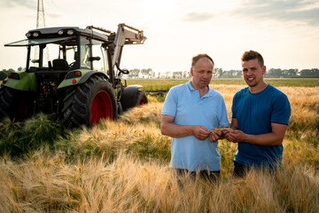 Landwirt mit seinem Sohn im reifen Getreidefeld, im Hintergrund steht ein Traktor.