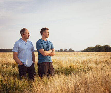 Zwei Landwirte stehen in einem reifen Getreidefeld und blicken in die Ferne.