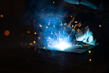 Metal welder works with a steel welder in a factory with protective equipment. Manufacture of metal structures and repair and construction services according to the concept of manual labor.