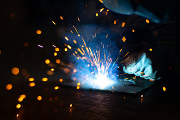 Fototapeta na wymiar Metal welder works with a steel welder in a factory with protective equipment. Manufacture of metal structures and repair and construction services according to the concept of manual labor.