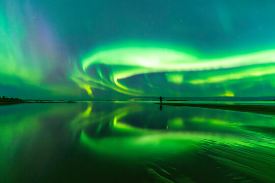 Northern lights reflected in water. Person standing on the bech. Storsand, Jakobstad/Pietarsaari Finland.