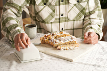 Man in a checkered shirt sitting at the table ready to eat traditional german christmas pastry christstollen on a marble cutting board, coffee mug, butter plate on the table cloth