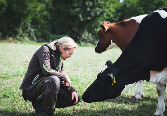 Junge Landwirtin in einer Kuhwiese, streichelt eine Kuh.