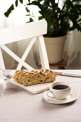 Traditional german christmas pastry stollen on a marble cutting board, coffee mug, butter plate on the table cloth and scandy style kitchen chair in the back