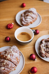 Delicious freshly brewed espresso coffee with a beautiful thick crema, standing on the wooden table with almond croissants, decorated with small red ornament Christmas balls, close up vertical image 