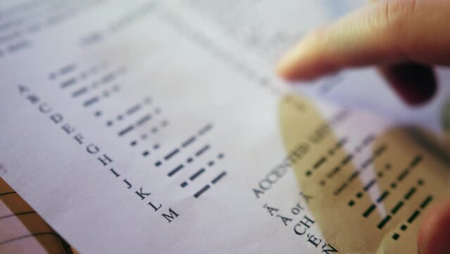 Man points finger on Morse code alphabet on page of educational book. Male person learns to communicate using telegraph closeup