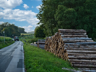 Fototapeta na wymiar Stack of logs next to a road with a tractor approaching in the background on a nice day