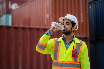 Workers or engineers drink water to quench their thirst at the container yard. Working on hot days. The concept of transportation in a container warehouse. - obrazy, fototapety, plakaty