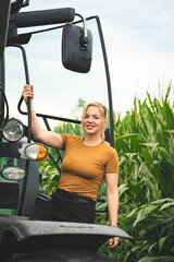 Freude am Arbeitsplatz - junge Landwirtin steigt auf einen Traktor auf, neben eines Maisfeldes.
