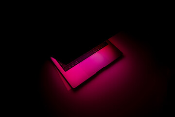 Laptop with backlit keyboard at night. Copy space. Illuminating pink neon light. Abstract...