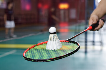 Badminton player holds racket and white cream shuttlecock in front of the net before serving it to...