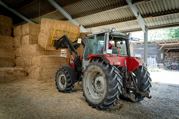  Landwirt mit Traktor und Frontlader beim Stapeln von großen Strohballen in einer Strohhalle.