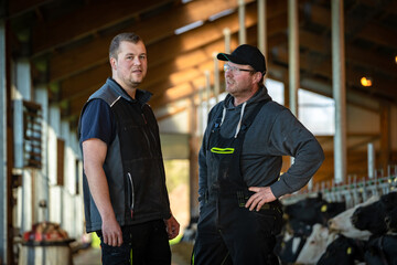 Vater und Sohn, beide Landwirte stehen zufrieden in ihrem modernen Kuhstall.