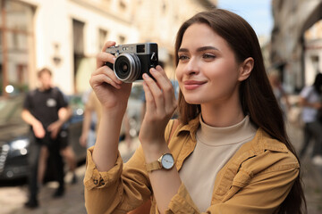 Young woman with camera taking photo on city street. Interesting hobby