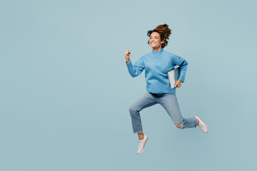 Fototapeta na wymiar Full body side view fun surprised smart young IT woman wear knitted sweater hold closed laptop pc computer run fast isolated on plain pastel light blue cyan background studio People lifestyle concept.