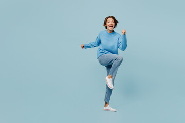 Full body young fun woman wear knitted sweater look camera doing winner gesture celebrate clenching fists say yes isolated on plain pastel light blue cyan background studio. People lifestyle concept.