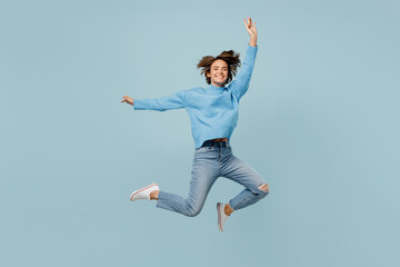 Full body overjoyed exultant young woman in knitted sweater look camera jump high with outstretched...