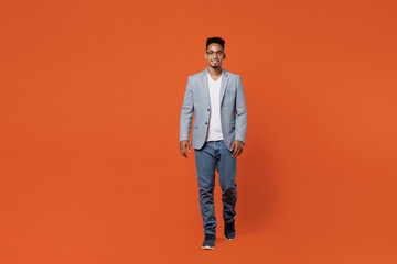 Full body happy successful young employee business man corporate lawyer wear classic formal grey suit shirt glasses work in office look camera go walk isolated on plain red orange background studio.