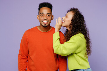 Young couple two friends family man woman of African American ethnicity wear casual clothes together whisper gossip and tells secret behind her hand sharing news isolated on plain purple background