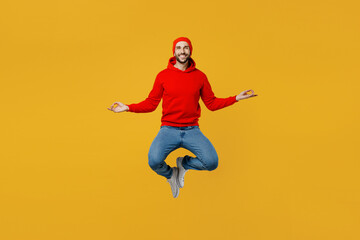 Full body young caucasian man wear red hoody hat look camera jump high hold spreading hands in yoga...