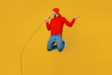 Full body young singer man wear red hoody hat jump high sing song in microphone have fun at karaoke...
