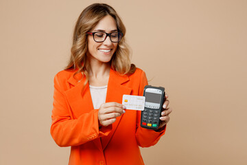 Young employee business woman corporate lawyer 30s wear classic formal orange suit glasses work in office hold bank payment terminal to process acquire credit card isolated on plain beige background.