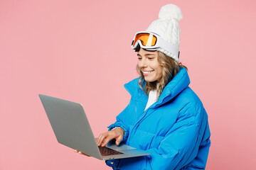 Snowboarder IT woman wear blue suit goggles mask hat ski padded jacket work hold use laptop pc computer isolated on plain pastel pink background. Winter extreme sport hobby weekend trip relax concept.