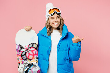 Snowboarder fun woman wear blue suit goggles mask hat ski padded jacket stand akimbo point aside on area isolated on plain pastel pink background Winter extreme sport hobby weekend trip relax concept © ViDi Studio