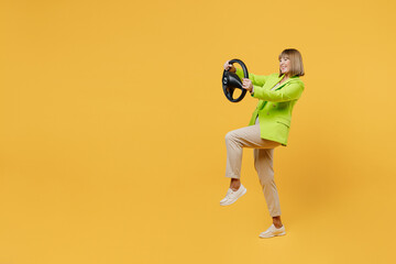 Full body side view fun elderly happy woman 50s years old wear green jacket white t-shirt hold steering wheel driving car isolated on plain yellow background studio portrait. People lifestyle concept.